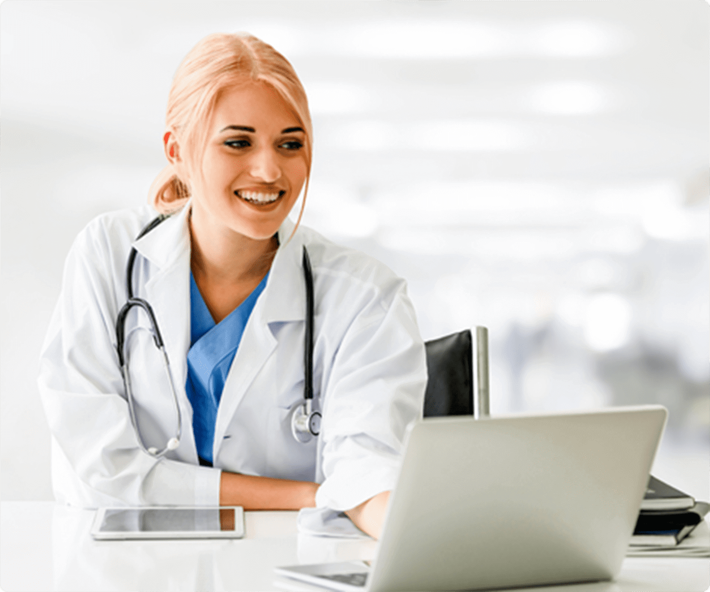 Female doctor sits at a desk smiling at her laptop screen